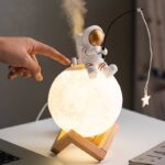 Petite décoration d'astronaute sur une lune lumineuse, illuminant une table, avec un fond neutre, idéale pour une décoration scientifique ou thématique.