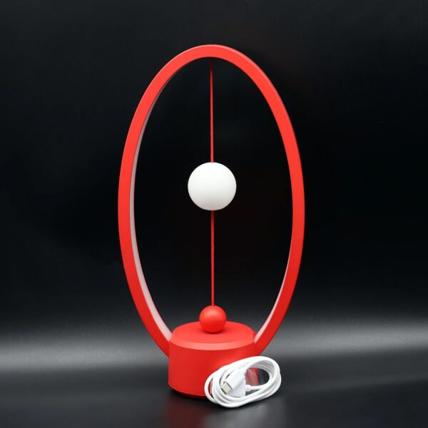 Horloge de bureau design moderne avec cadre ovale rouge, deux sphères blanches et rouges suspendues, et câble d'alimentation inclus, parfait pour la décoration scientifique et contemporaine.