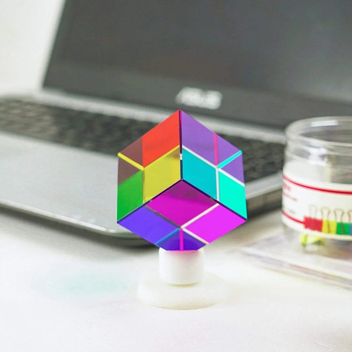 Cube coloré en 3D avec ordinateur portable en arrière-plan, illustrant un objet scientifique décoratif moderne et vibrant, parfait pour la décoration de bureau ou d'espace scientifique.