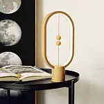 Lampe de décoration inspirée de la science, en forme d'orbite avec sphères dorées, posée sur une table noire avec un livre ouvert à côté.