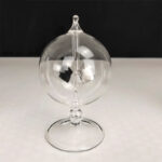 Boule à pendule en verre transparent avec mécanisme suspendu, décor scientifique élégant, sur fond noir et blanc.