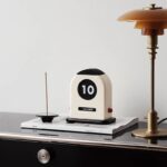 Rétrocalendrier de bureau vintage avec affichage numérique, placé sur une table avec une lampe et des magazines, décoration inspirée du style scientifique et rétro.