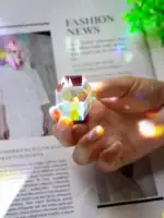 Objet scientifique en cristal coloré, tenu entre les doigts, avec un fond de magazine et une plante verte.