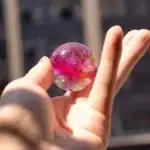 Boule en verre colorée et transparente tenue entre les doigts, avec un fond flou d'une scène urbaine. Idéal pour la décoration scientifique ou comme objet de collection.
