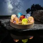 Collection de balles de cristal colorées illuminées, posées sur une surface rocheuse avec un ciel étoilé en arrière-plan, créant une ambiance magique et mystérieuse.