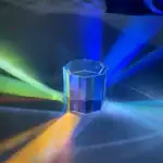 Pendentif en cristal hexagonal transparent avec effets lumineux colorés, projetant des reflets multicolores sur la surface environnante.