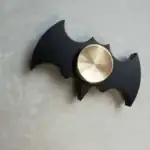 Accessoire de décoration inspiré de Batman, en forme de batarang avec un mécanisme de rotation en métal doré.