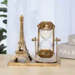 Sablier décoratif en laiton avec motif vintage, représentant un sablier classique avec un cadre en laiton antique, placé à côté d'une miniature de la Tour Eiffel en métal doré.