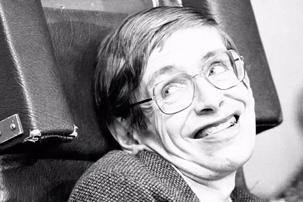 Vintage black and white photo of a smiling man with glasses, sitting in a chair, showcasing a humorous expression.
