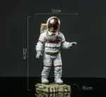 Figurine d'astronaute miniature avec casque doré, mesurant 22 cm de haut, 12 cm de large et 10 cm de profondeur, posée sur une base rocheuse, idéale pour décoration scientifique.