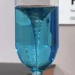 Pipette en liquide bleu versant dans un verre à pied, illustrant une expérience scientifique ou une démonstration de laboratoire.