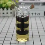 Vase en verre transparent avec spirale noire à l'intérieur, contenant un liquide jaune clair, décoratif et scientifique, avec bouchons en liÚge sur le haut.