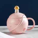 Vase décoratif en forme de tasse à thé avec motif spatial, comprenant un couvercle avec un petit astronaute doré. Parfait pour une décoration originale sur un bureau ou une étagÚre.