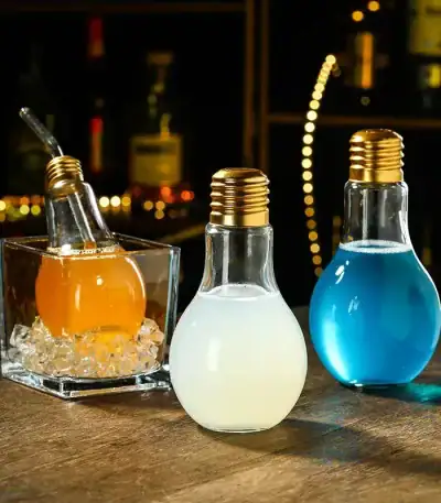 Trois ampoules décoratives remplies de liquides colorés (orange, blanc, bleu) sur une table en bois, ambiance chaleureuse et moderne.