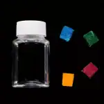 Bouteille en verre transparente avec un couvercle blanc, accompagnée de cubes de sucre colorés en bleu, vert, rouge et orange, sur fond noir.