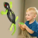 Jeune enfant souriant tenant une télécommande, interagissant avec un lézard robot lumineux fixé au mur.