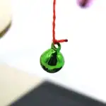 Boule de verre verte suspendue par un fil rouge, objet scientifique décoratif, mettant en valeur la transparence et la couleur vibrante du verre.