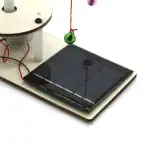 Panneau solaire illustrant une expérience éducative avec un objet scientifique, comprenant un dispositif solaire, un fil rouge, et une boule suspendue, parfait pour l'apprentissage de l'énergie solair.