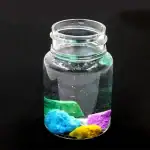 Vase en verre transparent contenant un liquide clair avec des substances colorées en dessous, créant un effet visuel scientifique et décoratif.