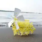 Véhicule scientifique miniature en plastique jaune avec hélice blanche, posé sur le sable près de la mer, illustrant un objet de décoration scientifique original et éducatif.