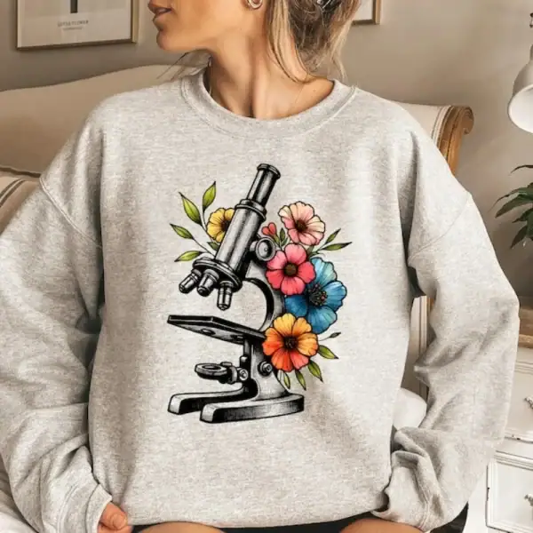 Microscope illustré avec des fleurs colorées sur un sweat gris, combinant science et nature dans un style moderne et tendance.