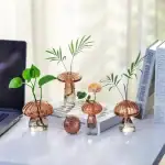 Vases en verre en forme de champignons avec plantes vertes et fleurs, décoration de bureau moderne et originale.