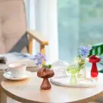 Vases en verre en forme de champignons avec fleurs colorées sur une table en bois, décoration de style scientifique et moderne.